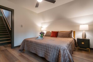 A bedroom with a bed, a nightstand, a lamp, a tray with items, and a staircase. - Alpine Evergreen | Upscale A-Frame | Pet Friendly Cabin in Helen, GA (Helen)