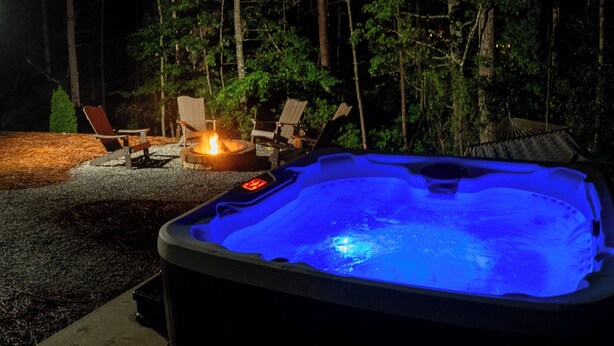 A hot tub with a blue light, surrounded by outdoor chairs and a fire pit. - Alpine Evergreen | Upscale A-Frame | Pet Friendly Cabin in Helen, GA (Helen)