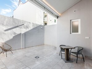 Patio esterno pulito e moderno con pavimento in piastrelle, un tavolo, due sedie e un faretto a parete.