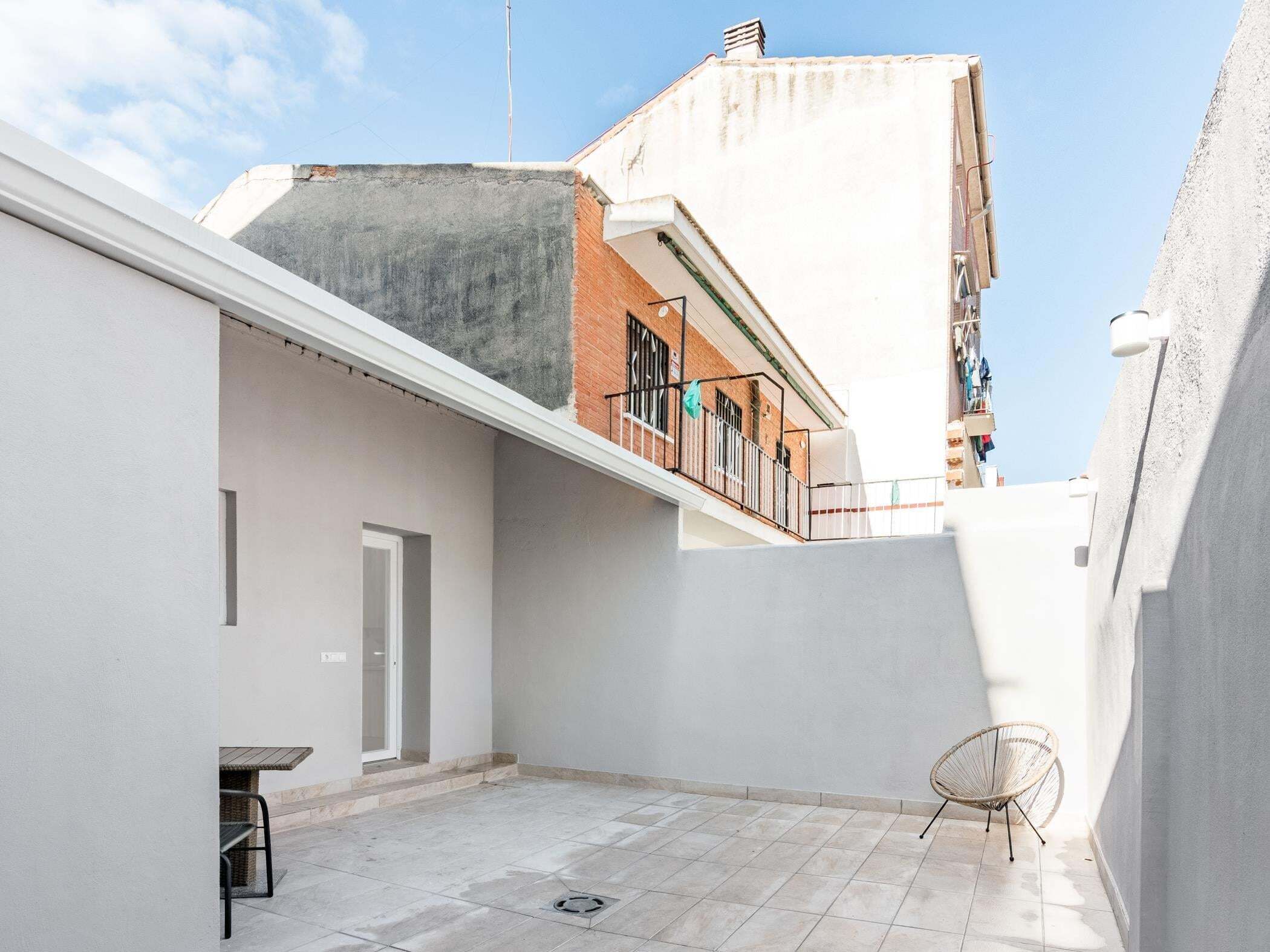 Una terraza en la azotea con un muro blanco, una puerta, una mesa pequeña y una silla.