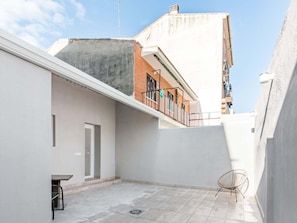 A rooftop terrace with a white wall, a door, a small table, and a chair.