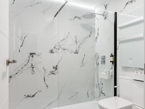 A modern bathroom with marble walls, a shower, a toilet, and a sink.