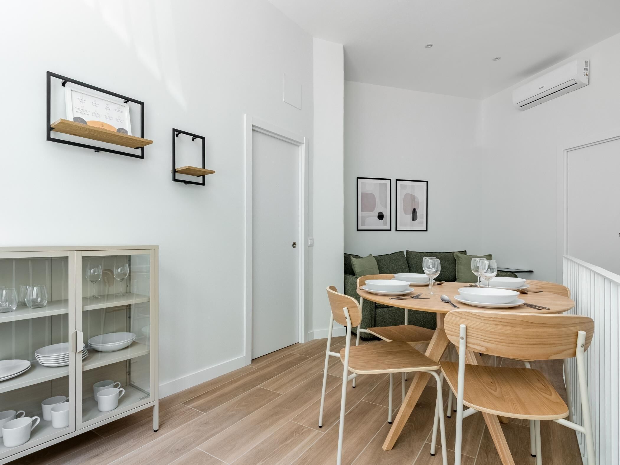 A modern dining area with a round table, chairs, and a glass cabinet with dishes.