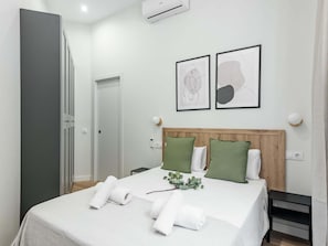 Ein Hotelzimmer mit einem Bett, einem Nachttisch, einer Wand-Klimaanlage und zwei gerahmten abstrakten Kunstwerken.