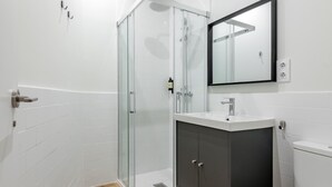 Un bagno moderno con box doccia in vetro, lavandino bianco, mobile contenitore scuro e WC bianco.