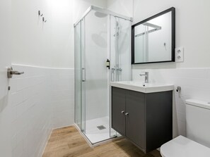 Ein modernes Badezimmer mit einer Duschkabine aus Glas, einem weißen Waschbecken, einem dunklen Schrank und einer weißen Toilette.