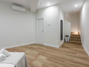 Ein moderner, minimalistischer Flur mit Holzboden, einer weißen Tür und einem Mülleimer.
