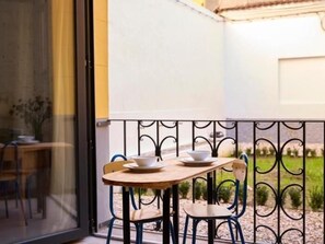 Un pequeño espacio exterior con comedor, una mesa, sillas, un vidrio y una barandilla de metal.