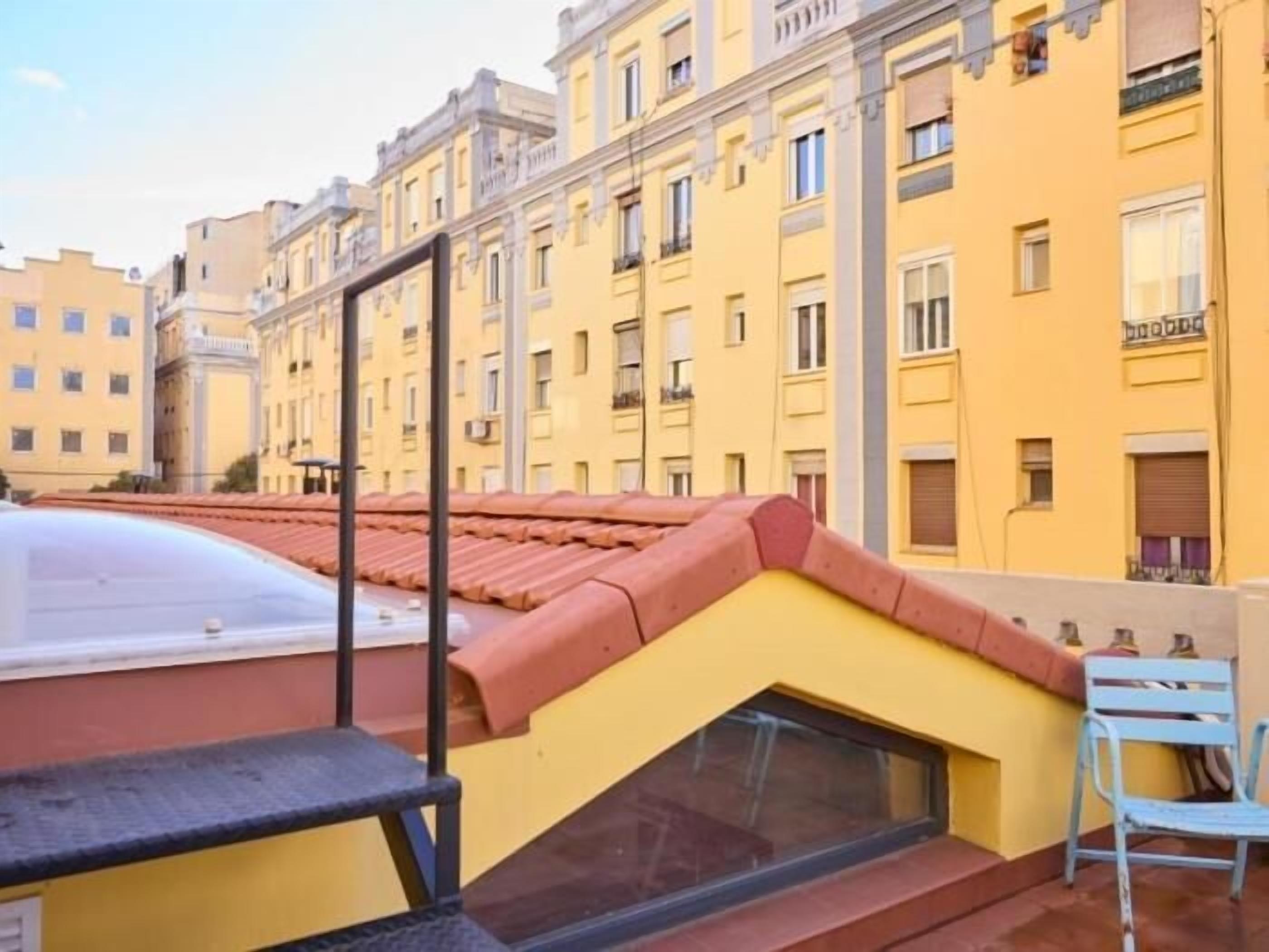 Un edificio amarillo con techo rojo, una ventana pequeña y una silla azul.