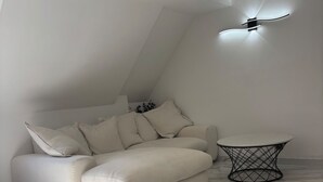 Ein modernes Wohnzimmer mit einem weißen Sofa, einem kleinen runden Tisch und einem Deckenventilator.