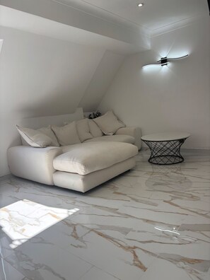 A modern living room with a white sofa, a small round table, and a ceiling fan. - Lavish, The White Apartment (Bury St Edmunds)