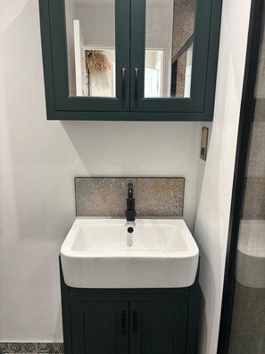 A bathroom with a white sink, dark green cabinets, and a mirror above the sink. - Lavish, The White Apartment (Bury St Edmunds)