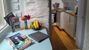 Eine Küche mit Holzausstattung, einer Arbeitsplatte und einer Schüssel mit Obst. Auf der Arbeitsplatte liegen Zeitschriften und ein Buch.