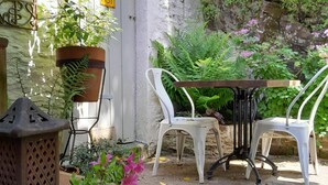 Eine Terrasse mit zwei weißen Stühlen, einem Tisch, einem Topfpflanzen und einer dekorativen Laterne.