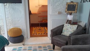 Ein gemütliches Wohnzimmer mit einem grauen Sofa, einem gemusterten Teppich und einem kleinen runden Hocker.