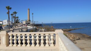 A coastal promenade with a lighthouse, palm trees, and a clear blue sky. - Studio Sleeps 4 With Terrace (Chipiona)