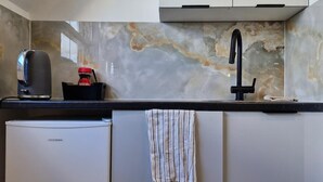 Eine Küche mit Marmor-Spritzschutz, einer Kaffeemaschine, einem Spülbecken und einem kompakten Kühlschrank.