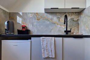 Eine Küche mit Marmor-Spritzschutz, einer Kaffeemaschine, einem Spülbecken und einem kompakten Kühlschrank.