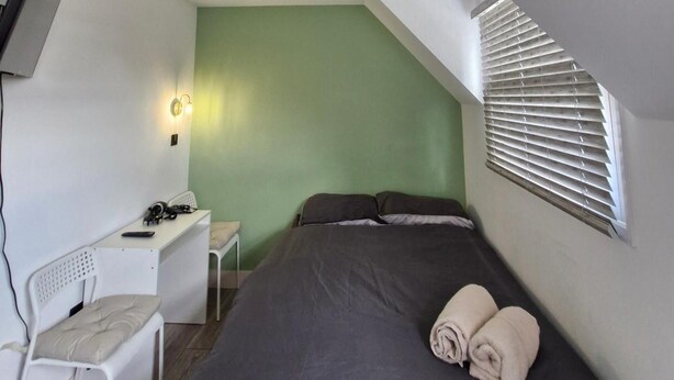 Ein Schlafzimmer mit einem Bett, einem Schreibtisch, einem Stuhl und einem Fenster mit Jalousien.