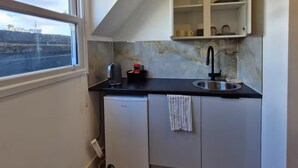Eine kompakte Küche mit Fenster, Spüle, kleinem Kühlschrank und einem Schrank über der Arbeitsfläche.