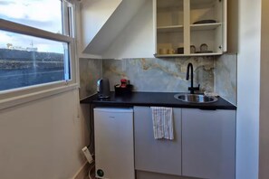 Eine kompakte Küche mit Fenster, Spüle, kleinem Kühlschrank und einem Schrank über der Arbeitsfläche.