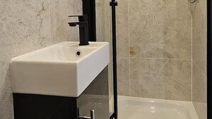Ein Badezimmer mit einer gläsernen Duschkabine, einem weißen Waschbecken und einem Spiegel.
