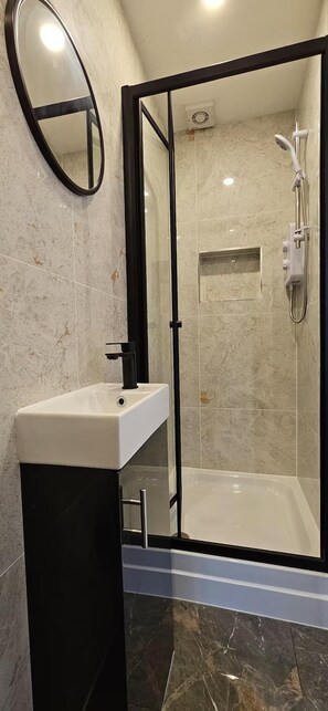 Ein Badezimmer mit einer gläsernen Duschkabine, einem weißen Waschbecken und einem Spiegel.