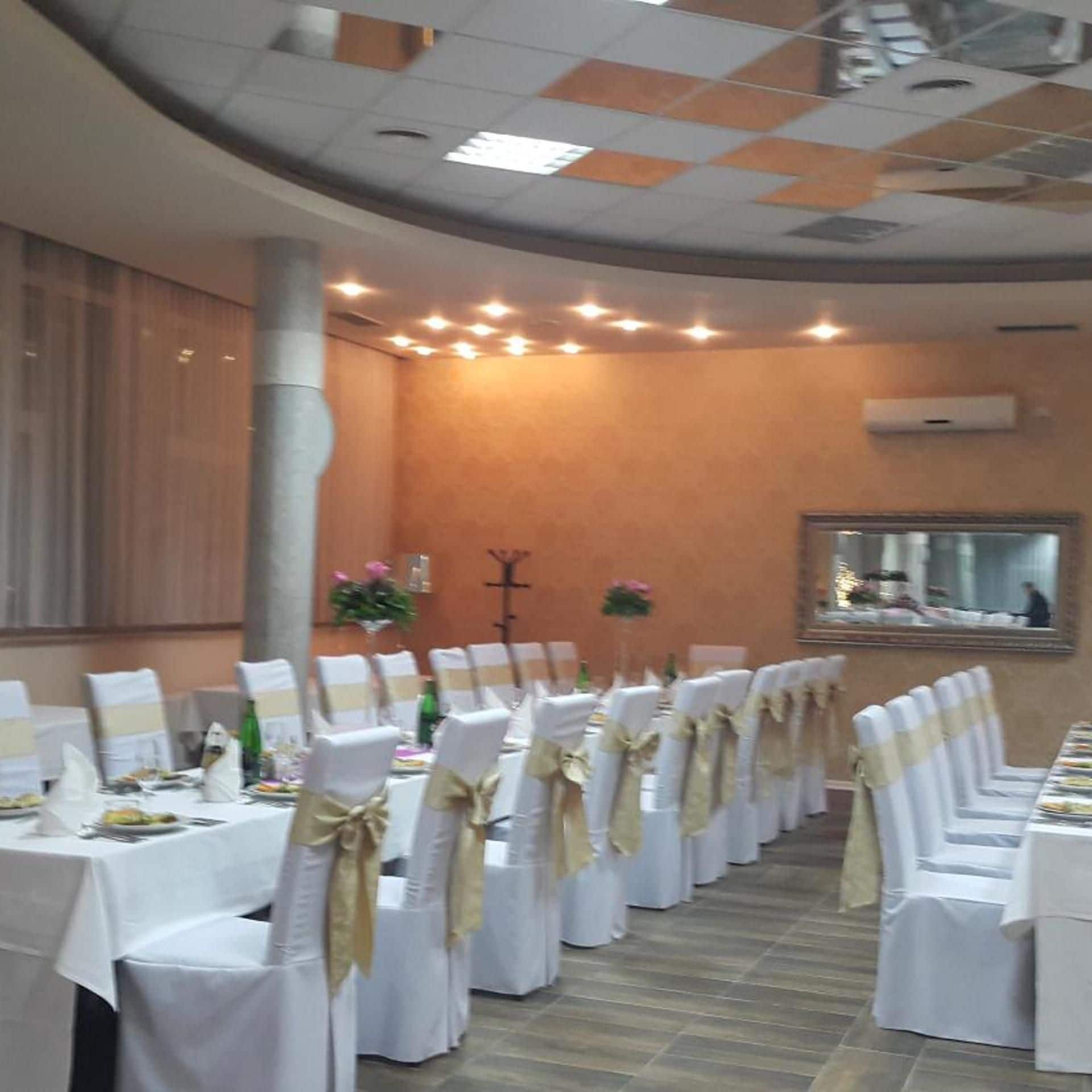 A banquet hall with rows of tables, white tablecloths, and chairs with gold sashes.