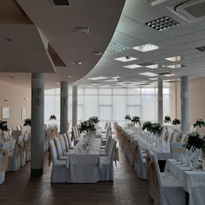 A spacious banquet hall with high ceilings, large windows, and rows of tables set for a formal event. - Park (Bihac)