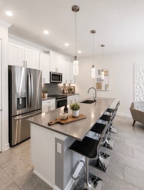 A modern kitchen with stainless steel appliances, a central island with bar stools, pendant lighting, and a geometric wall art piece. - Spacious 4-bedroom house with AC in pleasant Kissimmee (Kissimmee)
