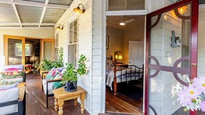 A cozy room with a bed, a small table, and a chair, a door leading to another room, and a window with curtains.