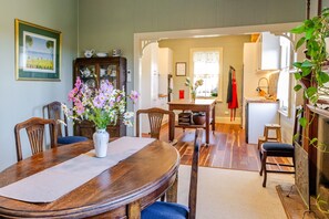A dining area with a wooden table, chairs, a vase of flowers, and a kitchen in the background.