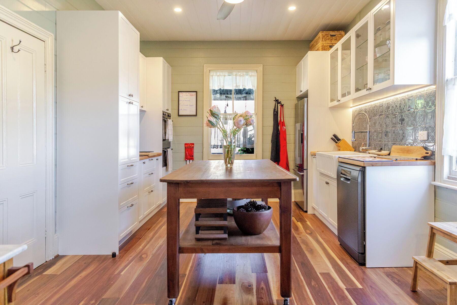A kitchen with a central island, wooden flooring, white cabinetry, and a window with a view.
