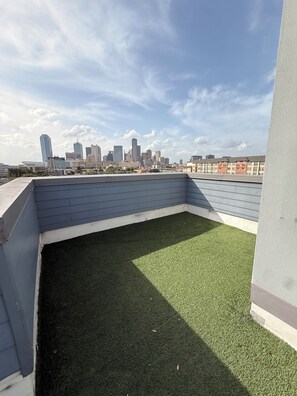 Un toit-terrasse recouvert de gazon synthétique, avec une vue sur les gratte-ciel de la ville en arrière-plan et un ciel dégagé.