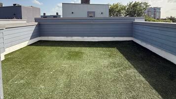 A rooftop with artificial grass, a flat roof structure, and a clear sky.