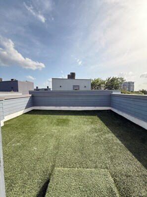 Una terraza con césped artificial, una estructura de techo plano y cielo despejado.