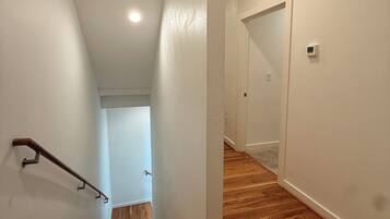 A hallway with wooden flooring, white walls, and a handrail on the left.