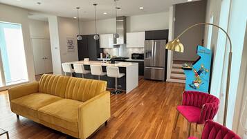 A modern living room with a yellow sofa, a red chair, and a kitchen area with a refrigerator and a blue Simpsons-themed cabinet.