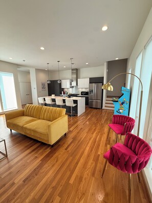 Una sala de estar moderna con un sofá amarillo, una silla roja y una zona de cocina con un refrigerador y un mueble azul con temática de Los Simpson.