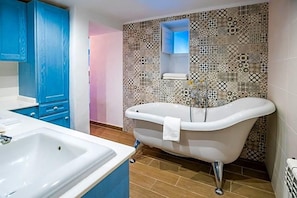 Un baño con una bañera independiente, un lavamanos y armarios azules.