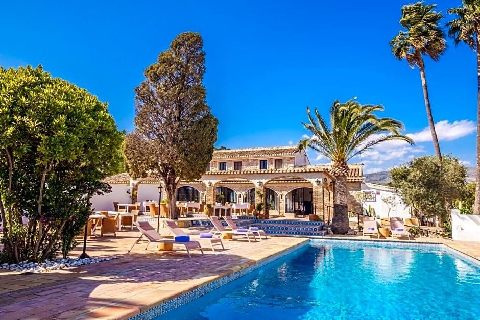 Un área junto a la piscina con sillones de descanso, piscina y un edificio con ventanas de arco y techo de tejas.