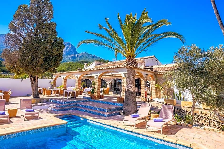 Un área junto a la piscina con sillones de descanso, una palmera y un edificio con arcos.