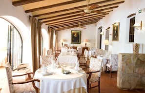 Un comedor con mesas redondas, sillas y un ventilador de techo.