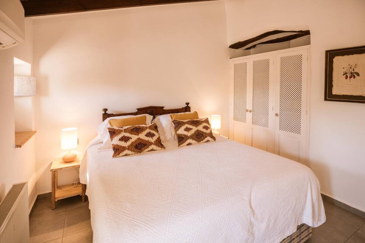 Ein Schlafzimmer mit einem Bett, zwei Nachttischlampen, einem Holz-Kopfteil und einem an der Wand befestigten Kleiderschrank.