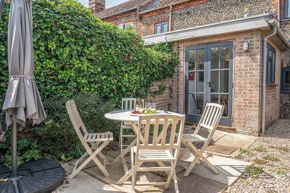 A patio with a round table and four chairs, a bottle of wine, and a plate of grapes.