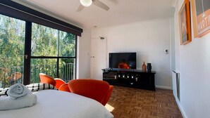 Una sala de estar moderna con un ventanal grande, ventilador de techo, televisor de pantalla plana y mueble de entretenimiento negro.