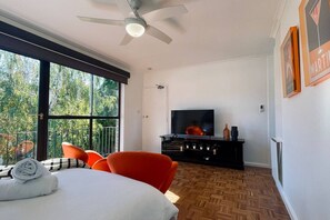 A modern living room with a large window, a ceiling fan, a flat-screen TV, and a black entertainment unit.