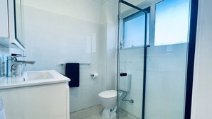 Un baño moderno con cabina de ducha de vidrio, inodoro blanco y lavabo con espejo.