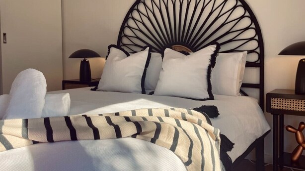 Una cama con cabecera de metal negro, ropa de cama blanca y mantas a rayas.