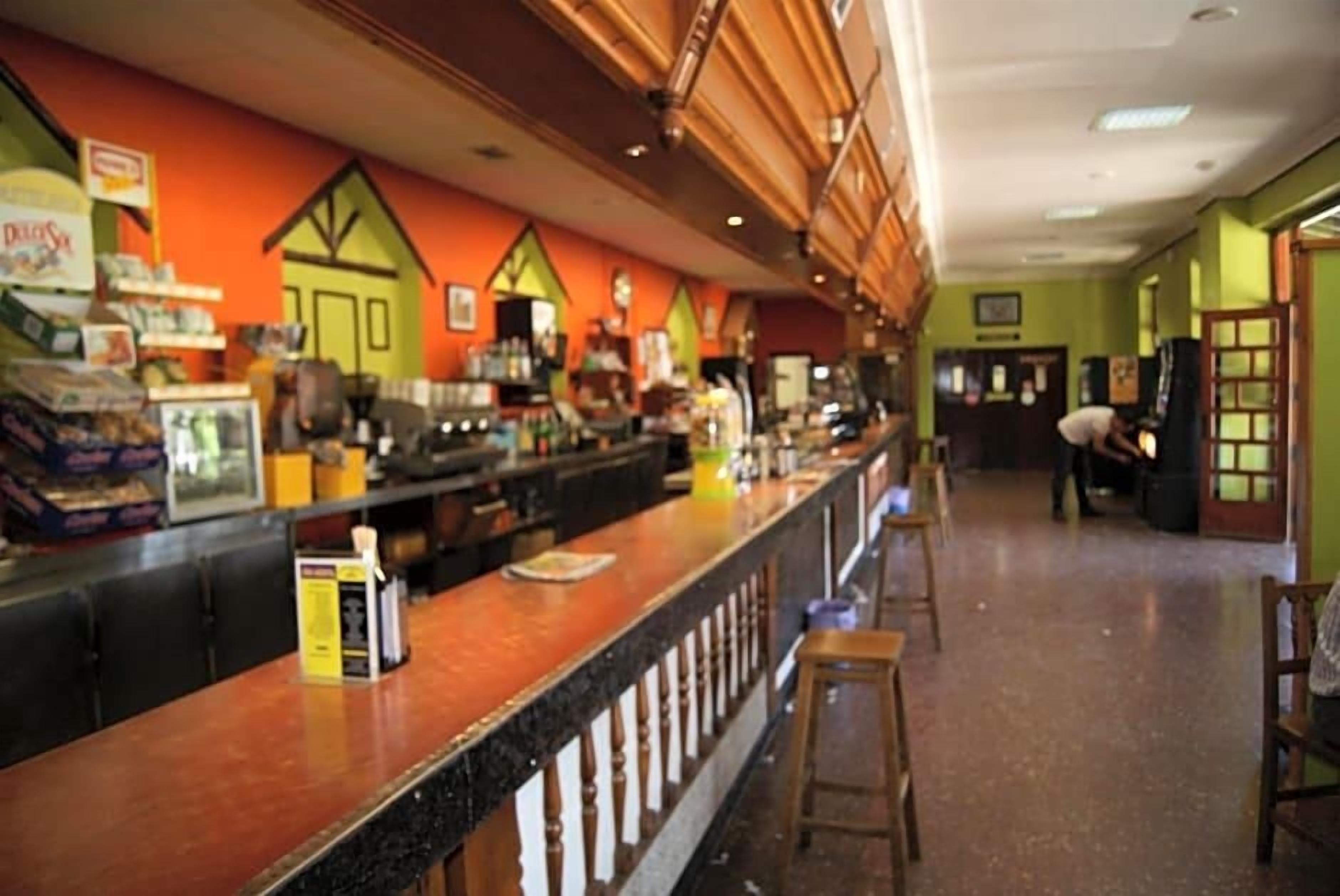 Un espace bar avec un comptoir, des tabourets et un mur vert orné d’un motif représentant une maison.